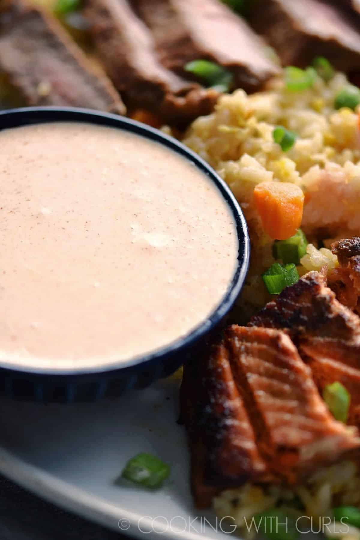 Yum Yum Sauce in a small bowl surrounded by sliced steak, salmon, and fried rice.