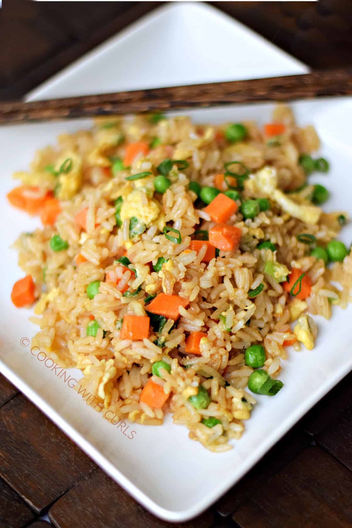 Rice mixed with soy sauce, scrambled eggs, peas, carrots, and green onions on a square plate.