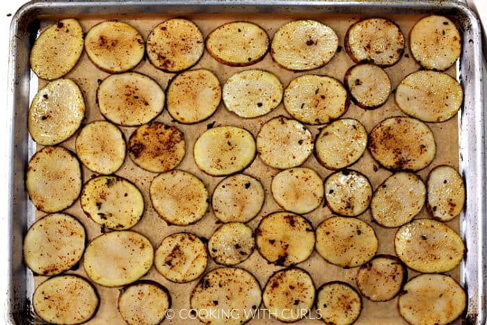 Seasoned potato slices lined up on a parchment paper lined baking sheet. 