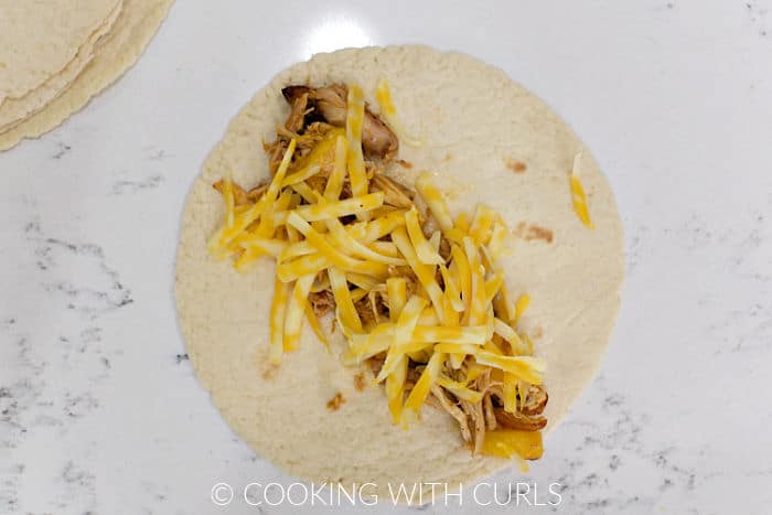 Shredded cheese over the peach and chicken filling down the center of a flour tortilla. 