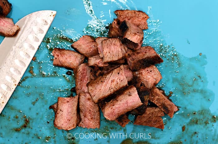 Steak cut into pieces on a blue cutting board. 