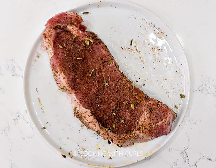 Steak rubbed with Mexican seasoning and sitting on a white plate. 