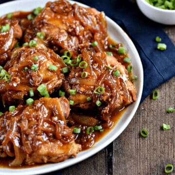 A plate full of chicken thighs topped with a brown onion sauce and chopped green onions.