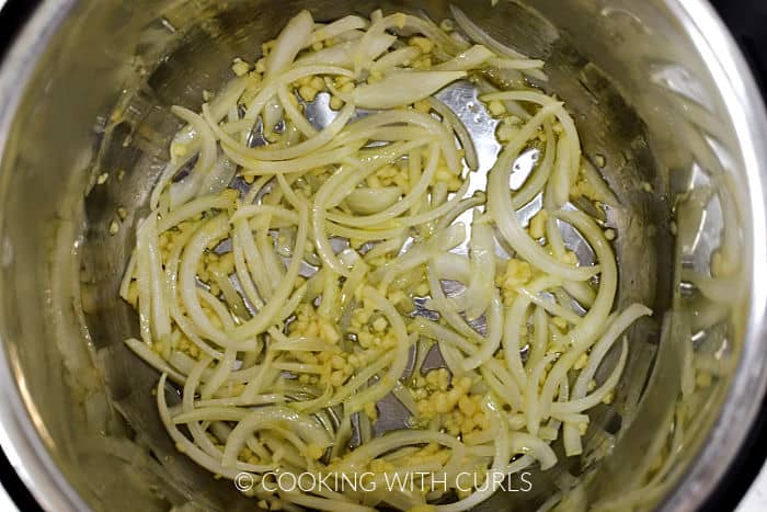 Minced garlic and sliced onion cooking in oil inside a pressure cooker liner. 