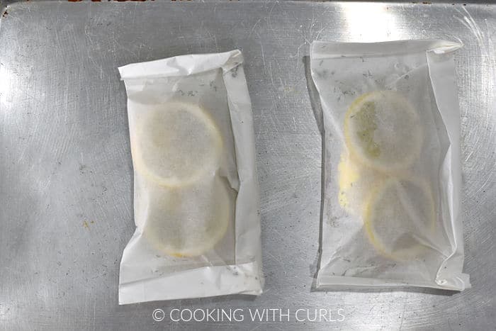 Two lemon topped cod fillets wrapped in parchment paper on a baking sheet. 