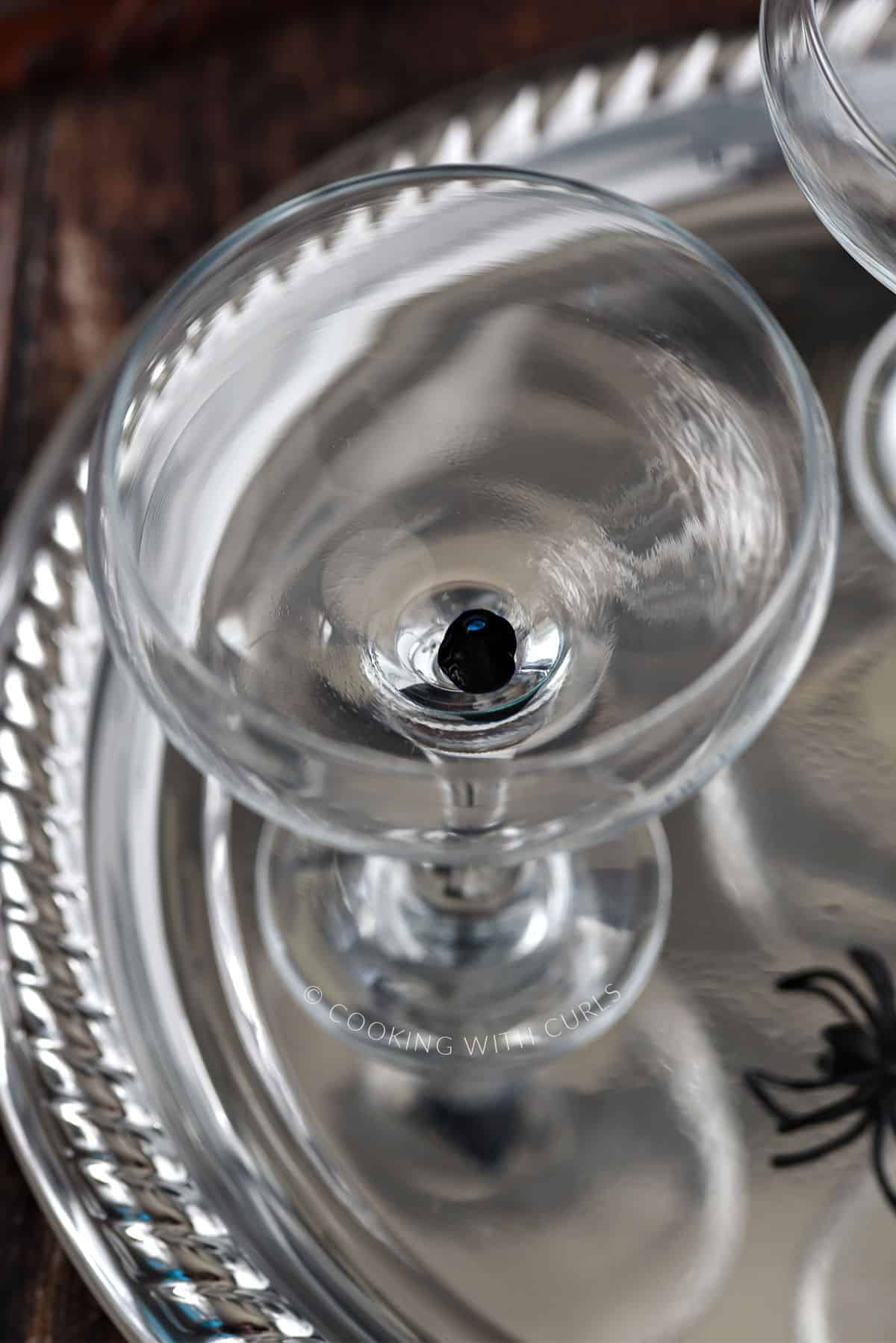 A drop of blue food coloring at the bottom of a cocktail glass sitting on a silver tray. 