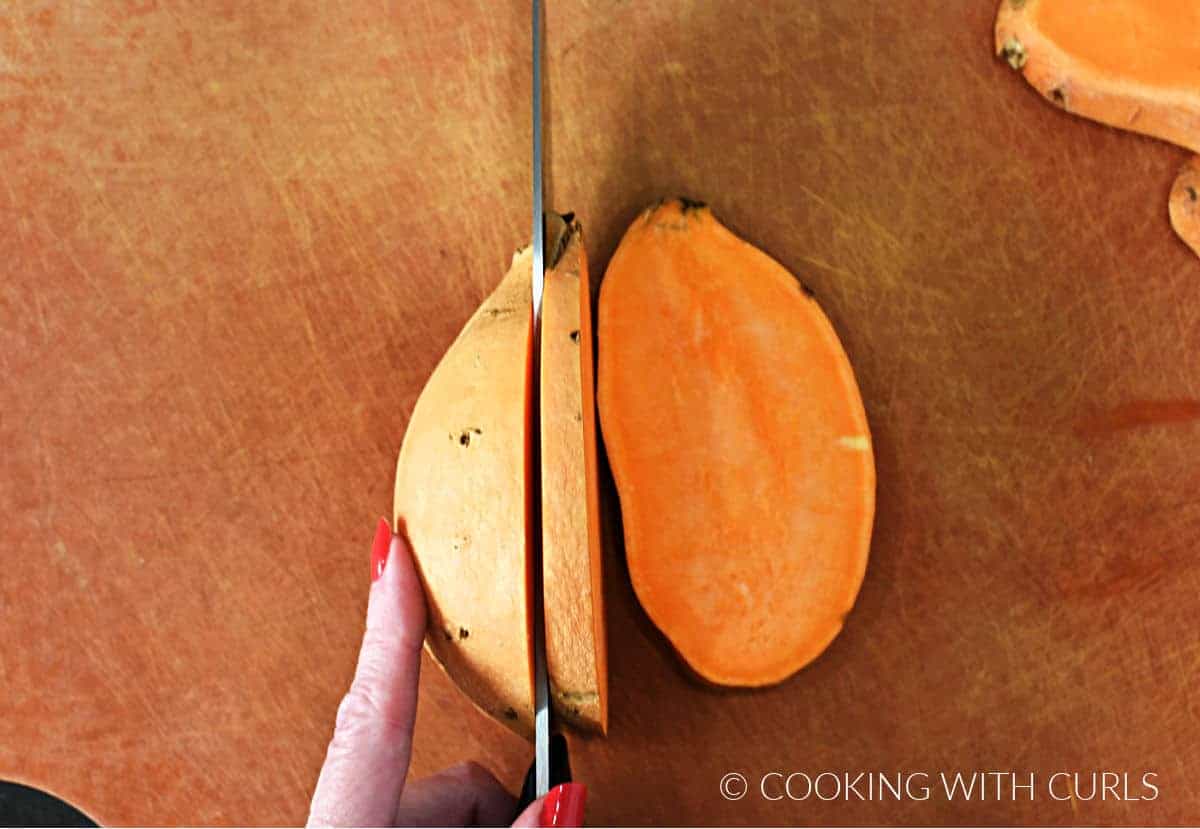 A hand holding a knife to cut thick slices in a sweet potato.