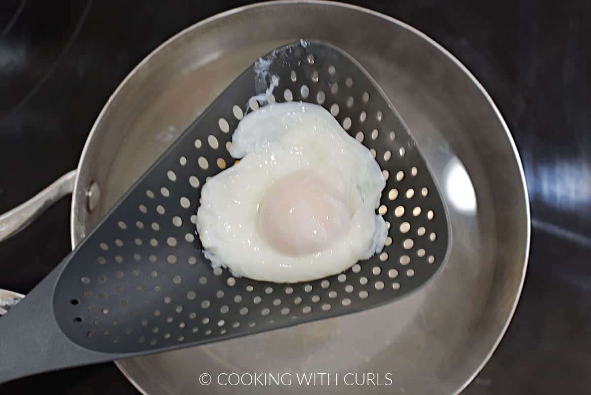 Poached egg in a strainer spoon over a pan of simmering water.