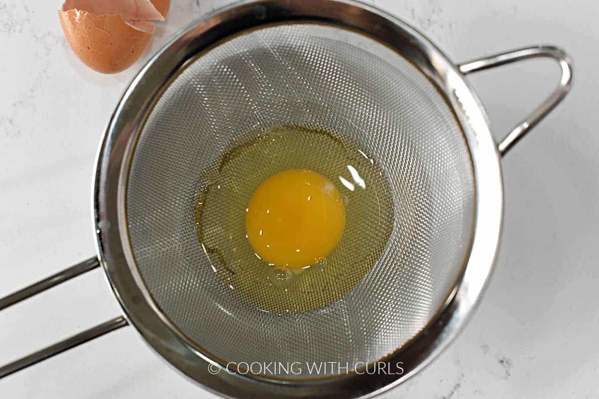 One egg in a fine mesh strainer over a small bowl.