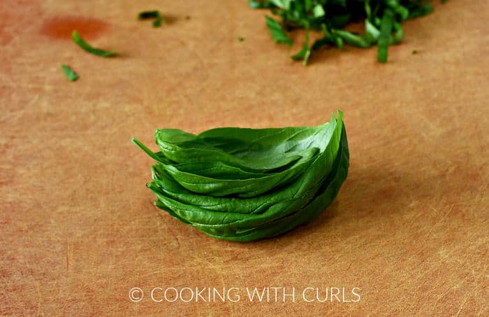 A stack of fresh basil leaves on a cutting board. 