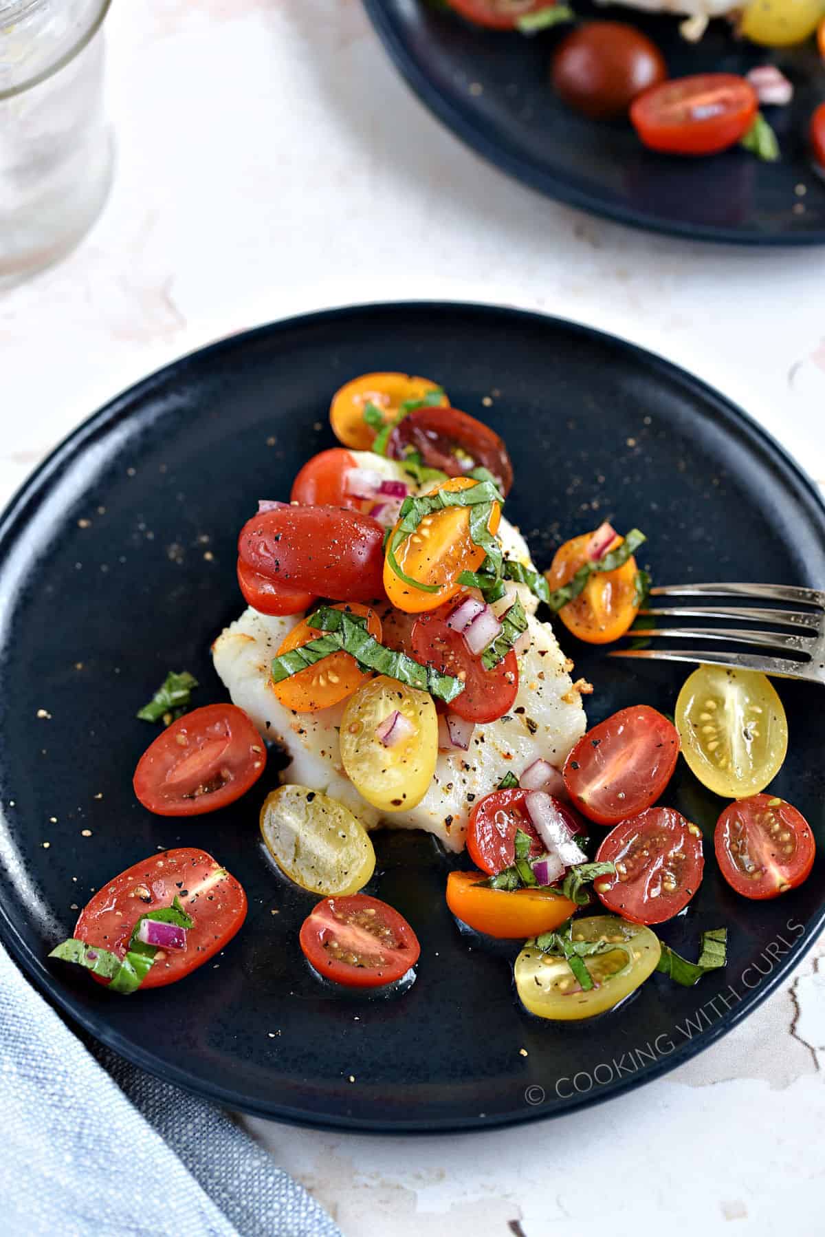 Cod filet topped with cherry tomato halves, strips of basil, red onion and black pepper.