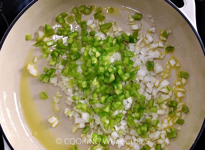 Chopped green pepper and onion in oil frying in a skillet. 