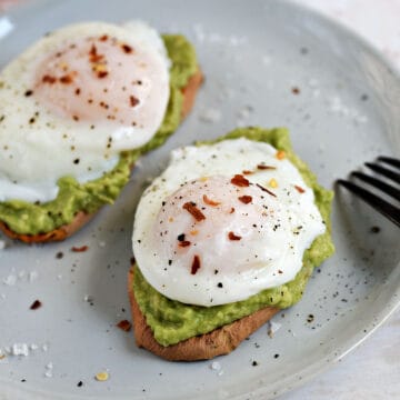 Close-up image of two poached eggs sprinkled with red pepper and salt flakes on avocado toast.
