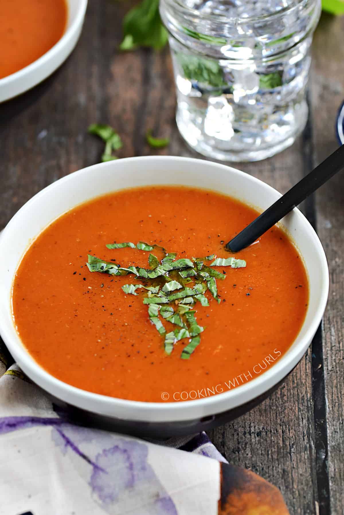 A bowl of tomato soup topped with shredded fresh basil and cracked black pepper.