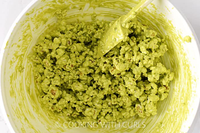 Popcorn coated with green chocolate in a large bowl with a silicone spatula. 
