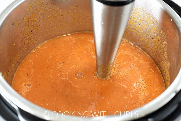 Soup being pureed with an immersion blender inside the pressure cooker. 