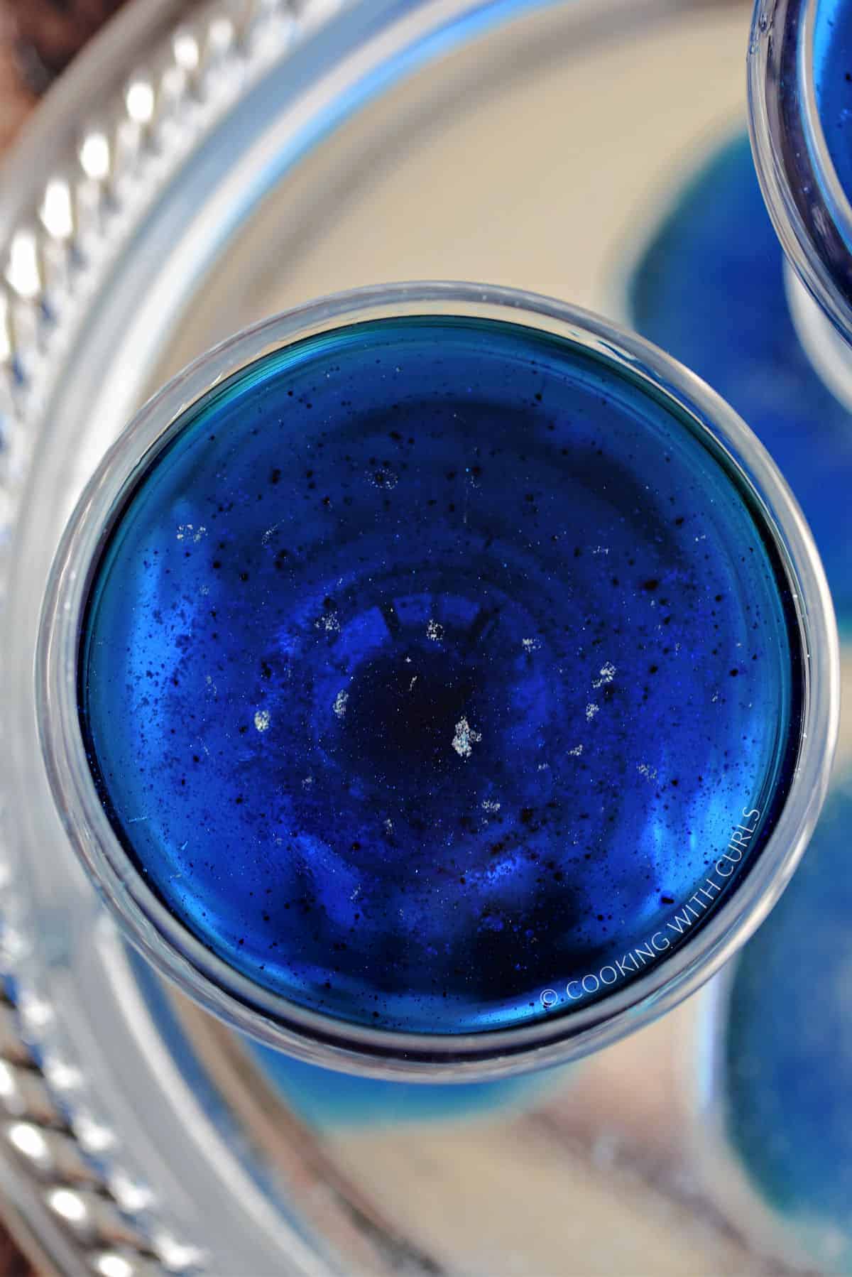 Specks of diamond dust floating on top of the blue cocktail in a coupe glass. 