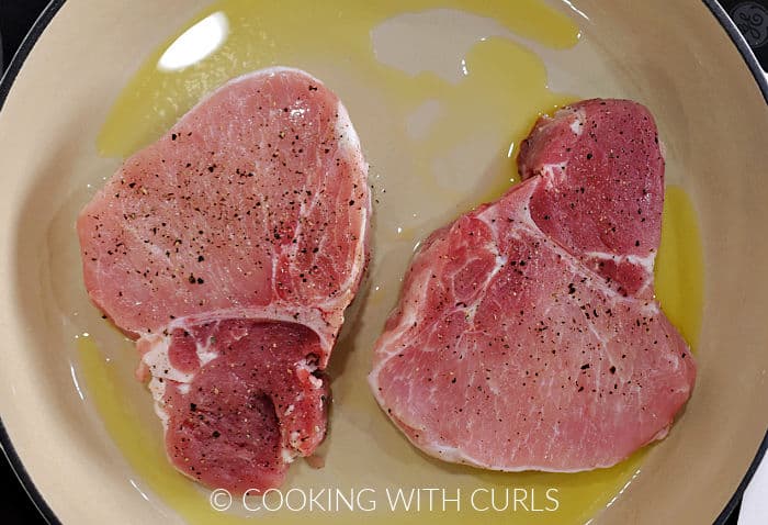 Two bone-in pork chops in an oiled skillet. 