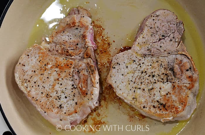 Two browned pork chops in a skillet. 