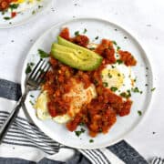 Two fried eggs topped with tomato sauce, and sliced avocado.