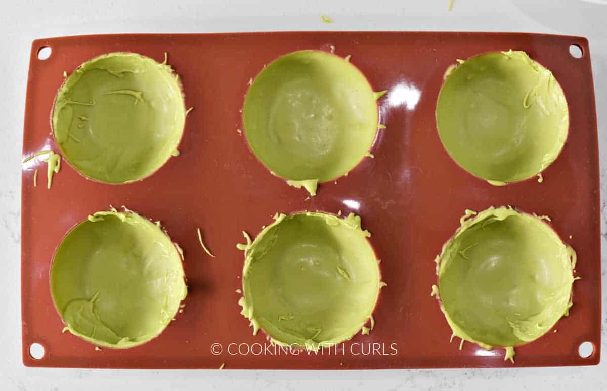 A silicone sphere mold with six cavities filled with melted green chocolate. 
