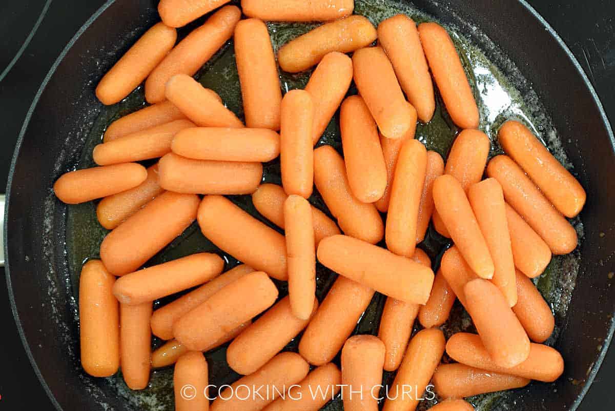 Baby carrots in the sweetened butter mixture in a skillet.