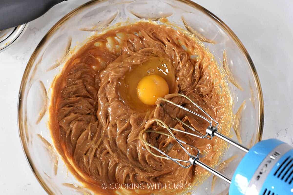 Butter and peanut butter beaten with a hand mixer in a large bowl with a raw egg broken into the center. 