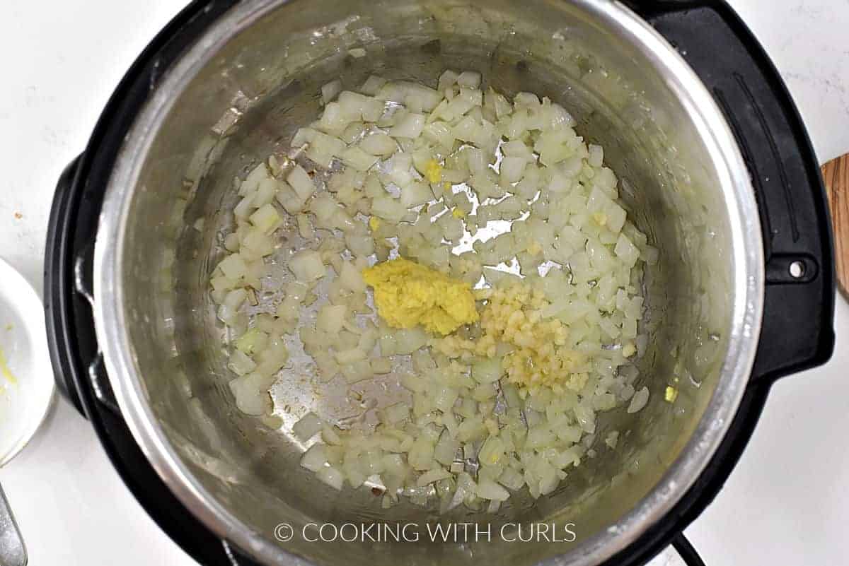 Chopped onion, minced garlic, and grated ginger in a pressure cooker.