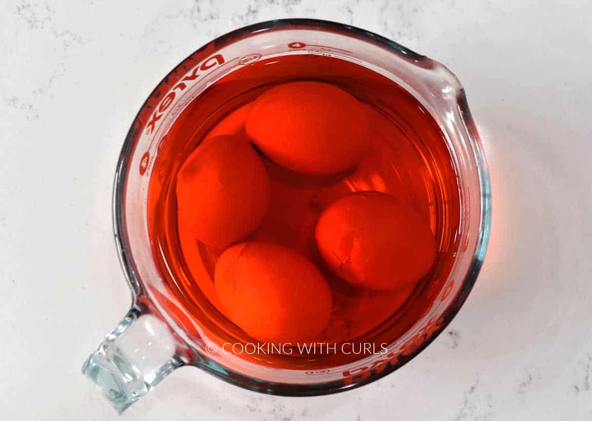 Four eggs in a measuring cup with red water. 