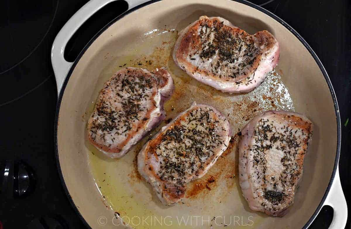 Four seasoned pork chops in a skillet. 