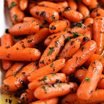 Baby carrots in a honey glaze and topped with chopped parsley on a white platter.