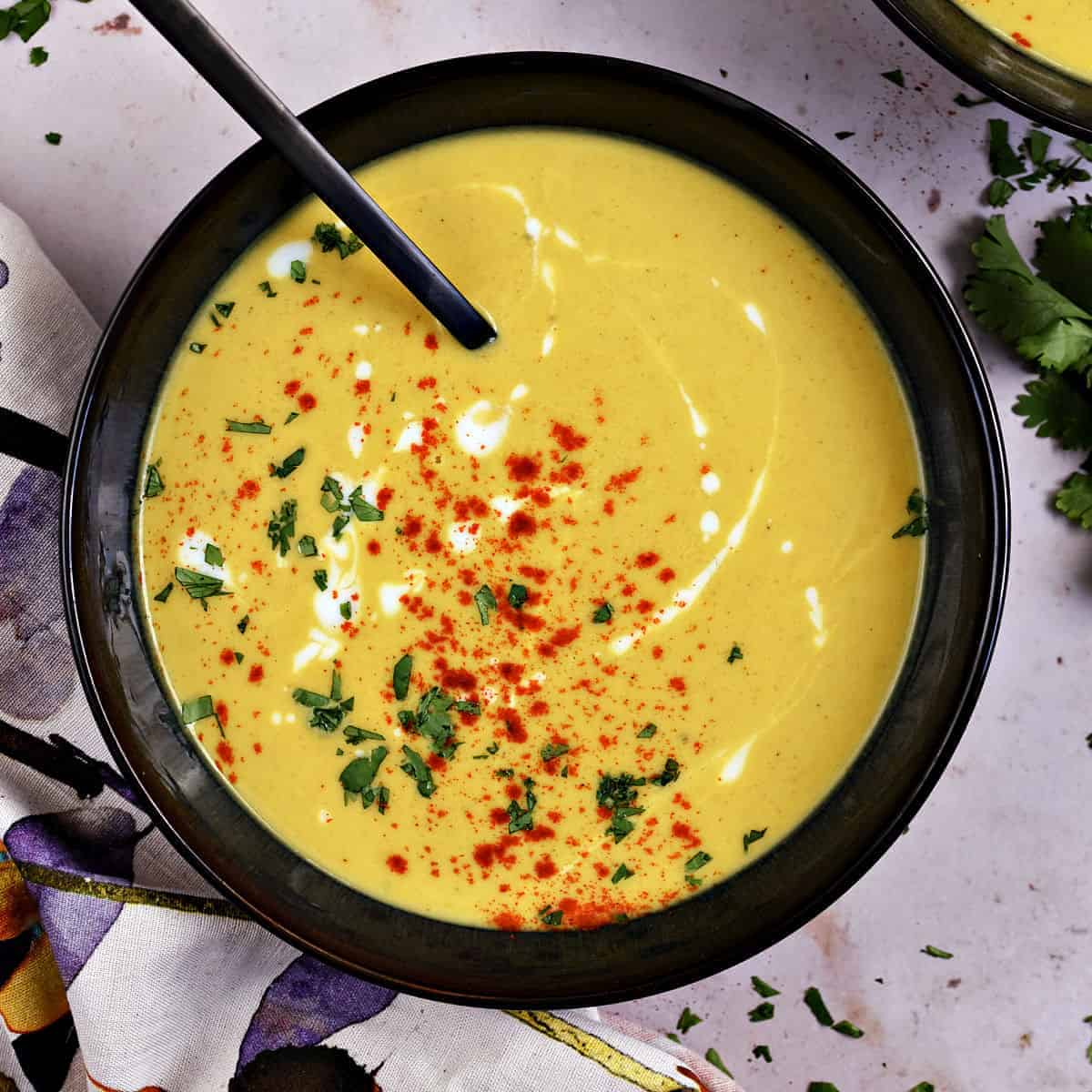 Butternut Squash soup in a dark bowl topped with paprika, chopped cilantro and kefir drizzle.