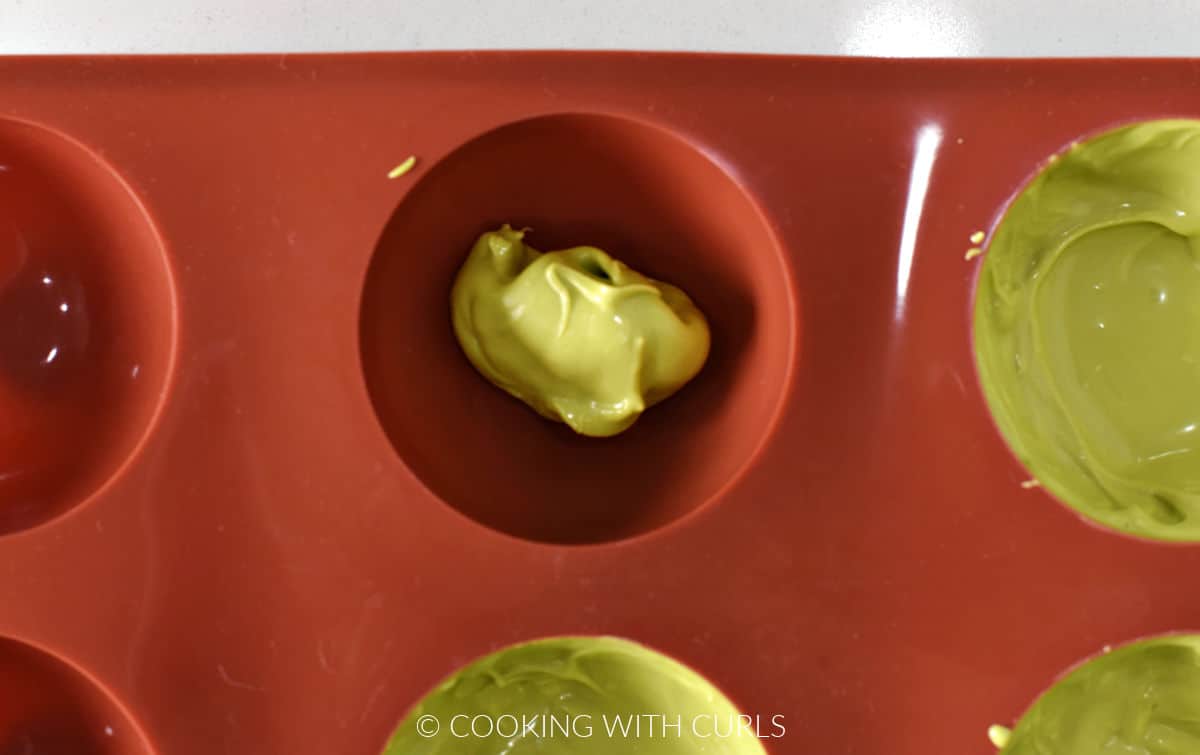 Melted green chocolate in the cavities of a silicone sphere mold.