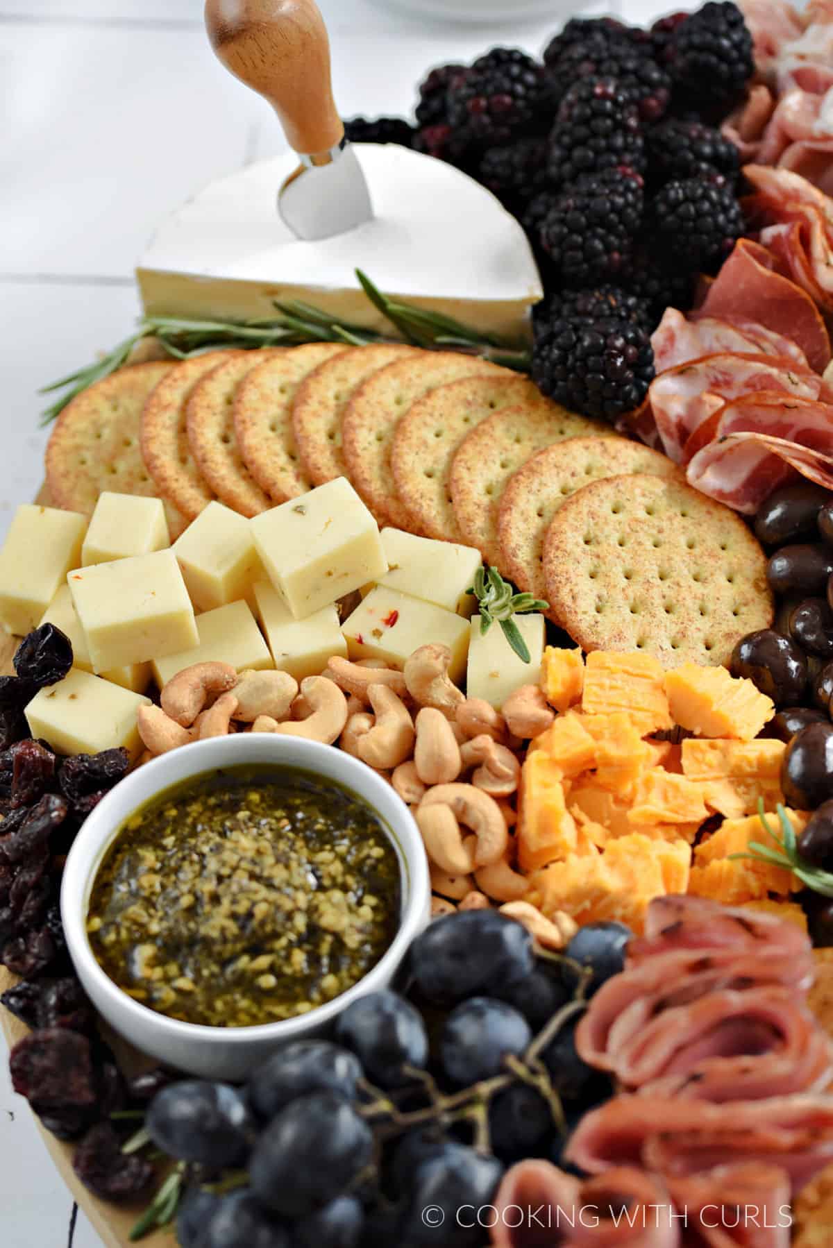 Blackberries, sliced meats, brie, bread slices, crackers, cheddar cheese, chocolate almonds, and mustard on a large appetizer board.