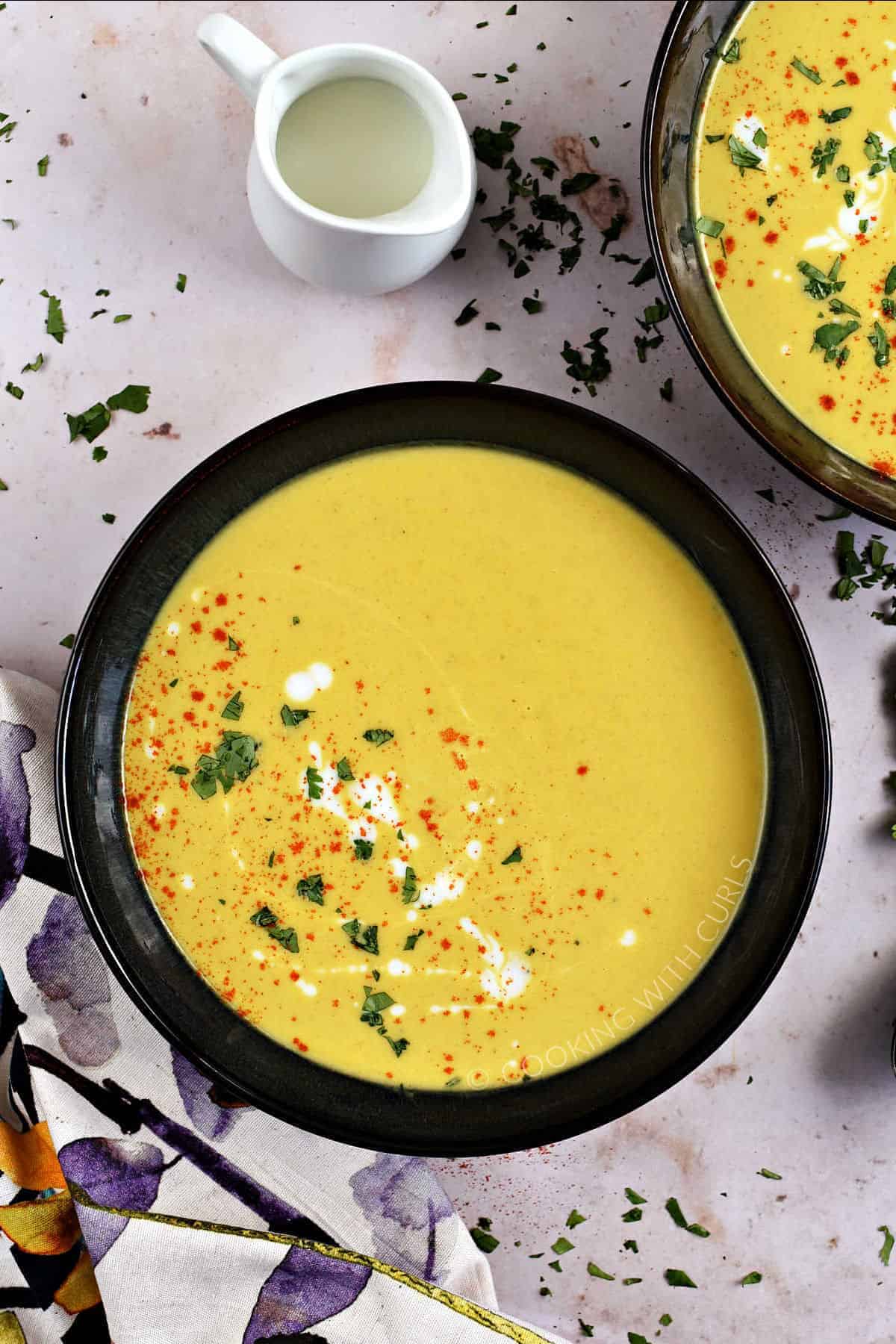 Two dark bowls filled with butternut squash soup sprinkled with paprika, cilantro, and kefir. 