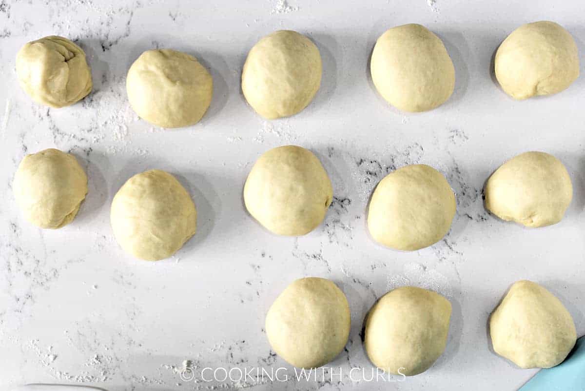 13 raw dough balls on a floured marble surface. 