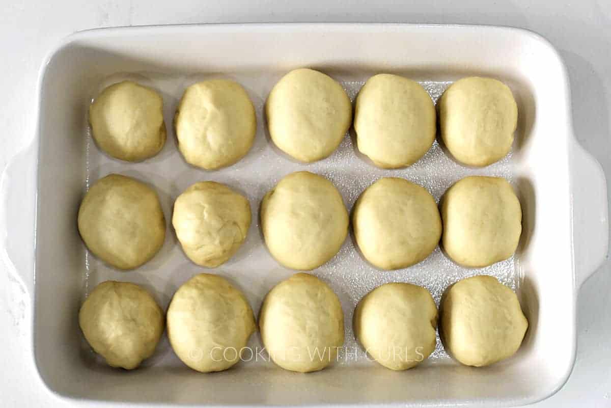 15 balls of raw dough in a white baking dish. 