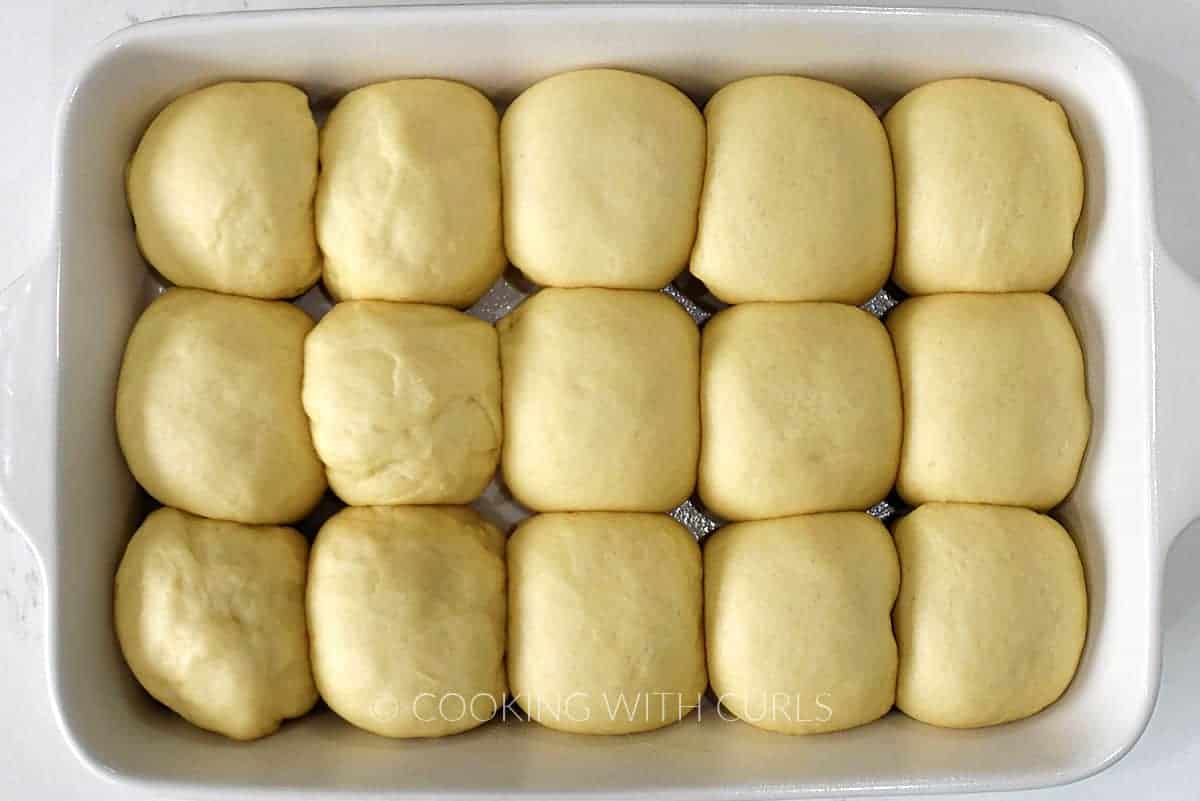 15 risen balls of dough in a white baking dish. 