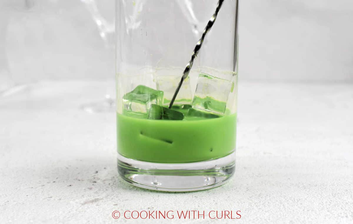 A grinch martini stirred in a glass with ice cubes. 