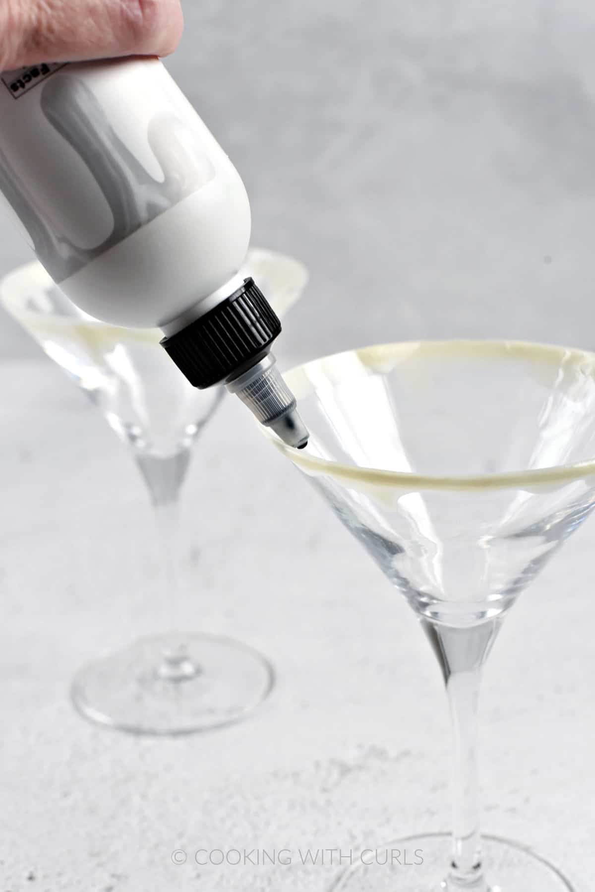 A hand pouring cake drip around the rim of a martini glass.