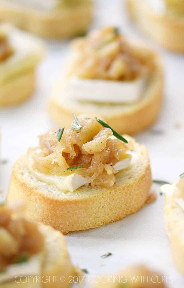 Multiple apple compote topped brie crostini on a platter.