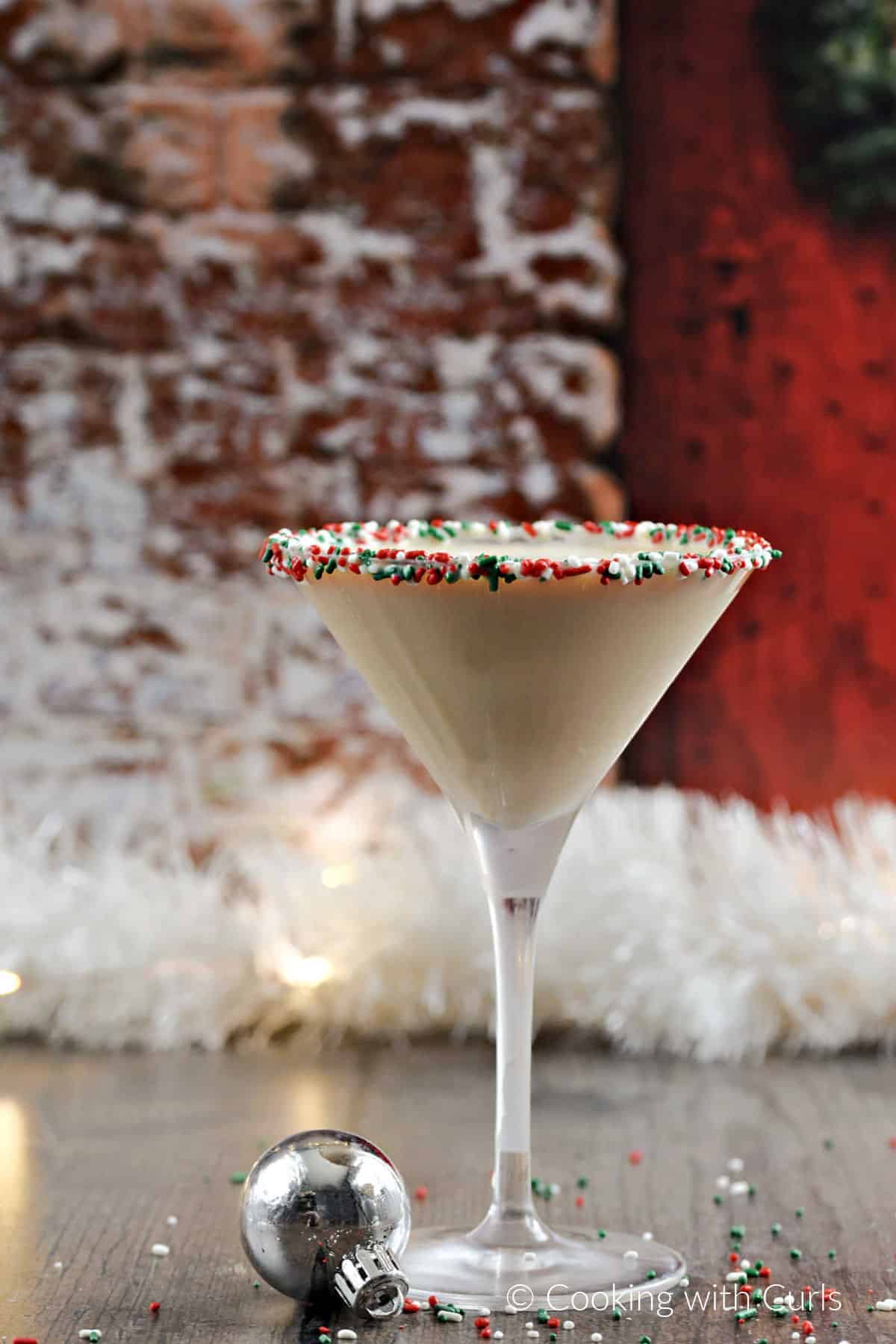 Christmas Cookie Martini with holiday sprinkles around the rim and a silver ornament at the base. 