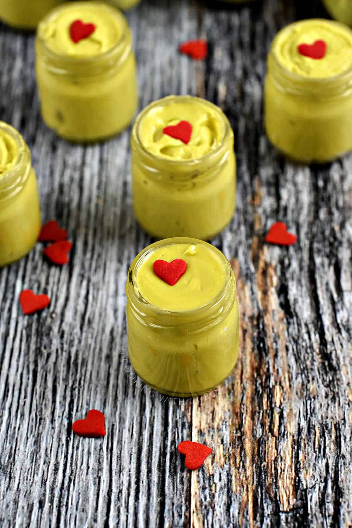 Five tiny jars of green Christmas fudge topped with a red heart candy.