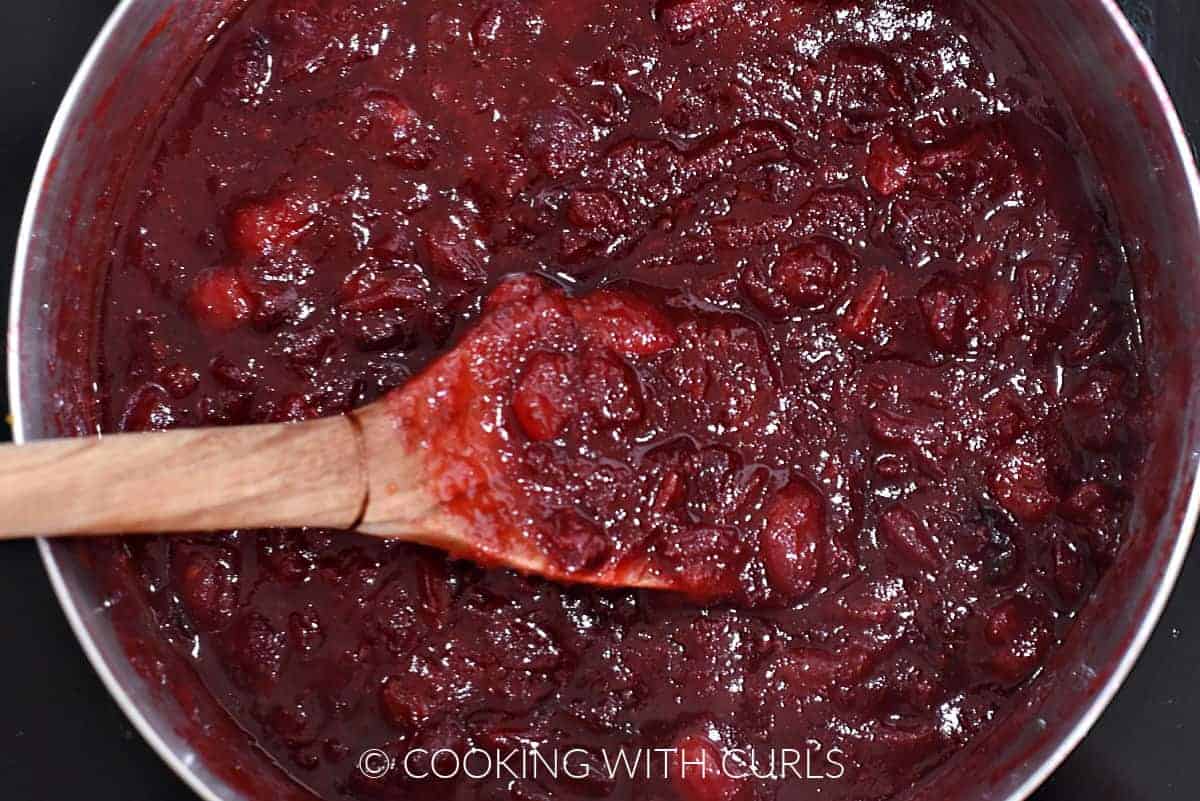 Cooked cranberry sauce stirred with a wooden spoon. 