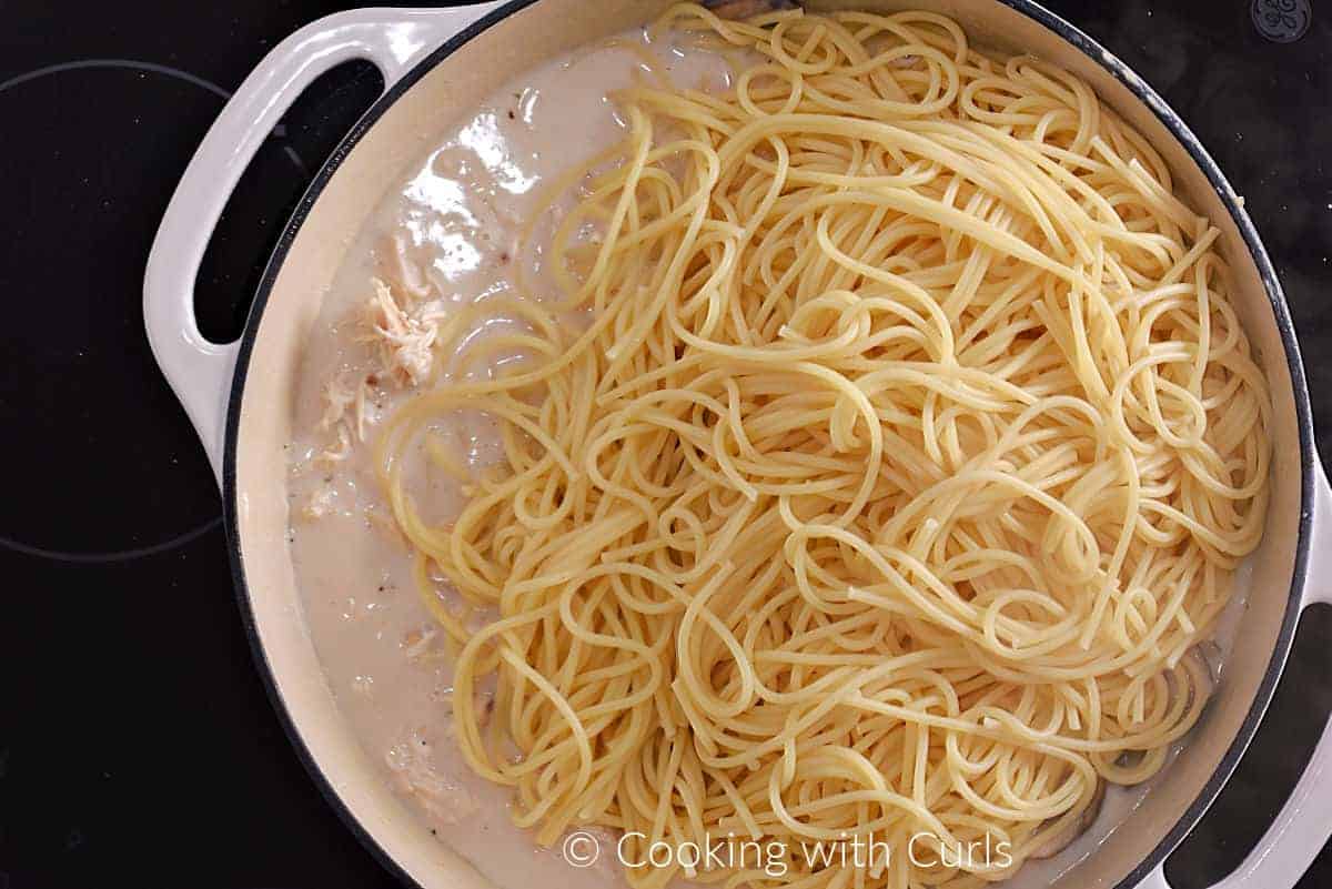 Cooked spaghetti noodles added to the chicken cream sauce in a skillet. 