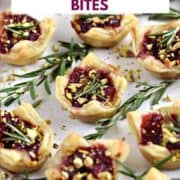 A platter of Puff Pastry Cranberry Brie Bites topped with fresh rosemary and chopped pistachios with title graphic across the top.