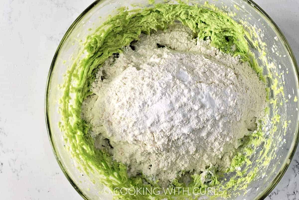 Flour, baking powder and soda added to the green butter mixture in a large glass bowl. 
