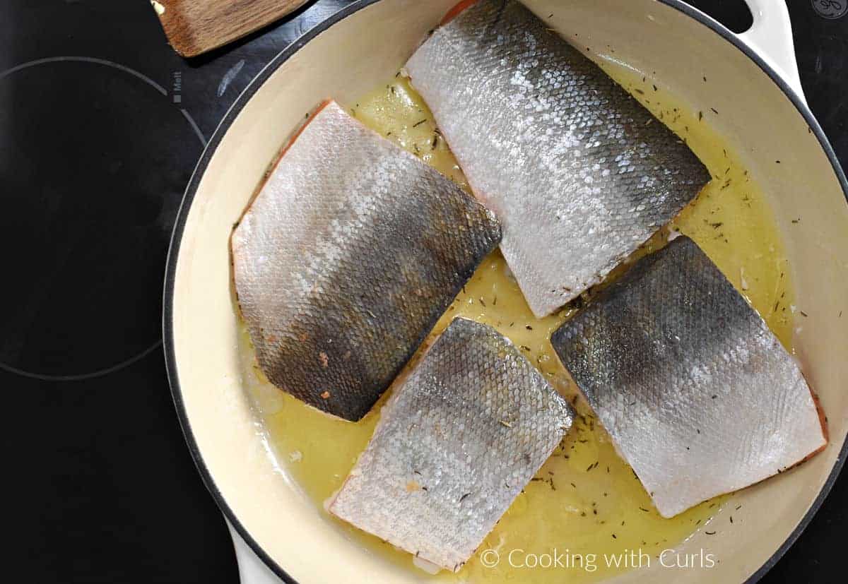 Four salmon filets skin-side up in a skillet with butter and oil. 