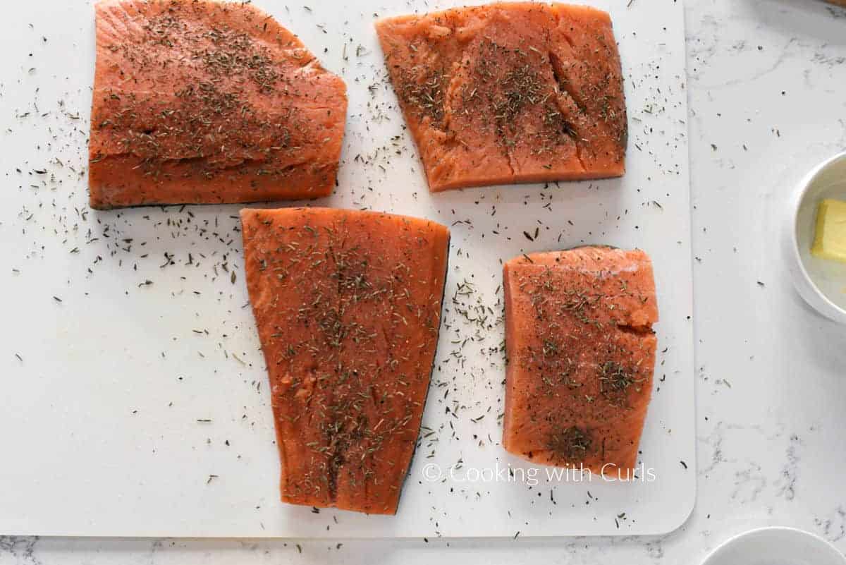 Four salmon filets topped with thyme leaves, salt and pepper. 