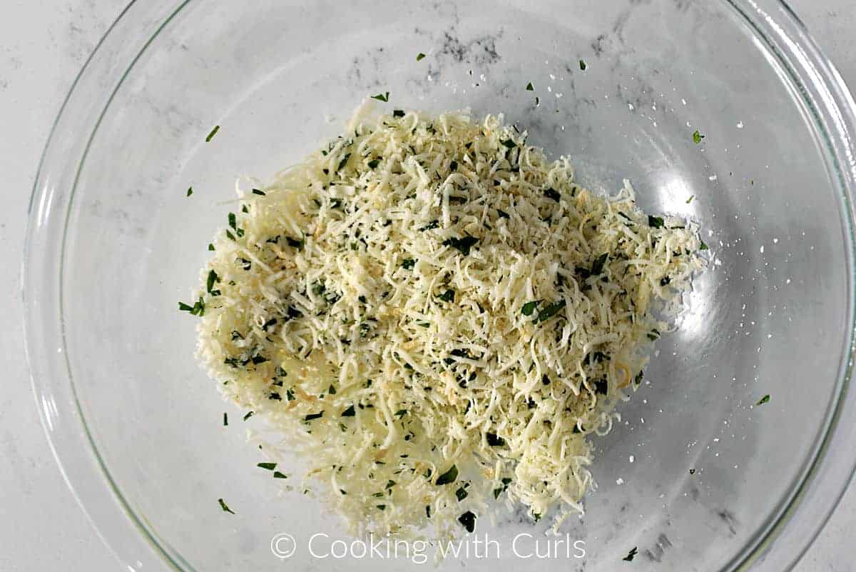 Grated mozzarella and parmesan cheese mixed with seasonings in a mixing bowl. 